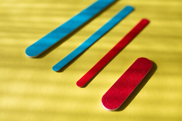 Set of red and blue disposable nail files on a yellow background. Tools for independent nail care.