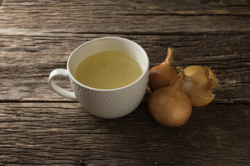 Bowl with clear, rich broth. White crockery on a wooden table at the age. Bow about a mug