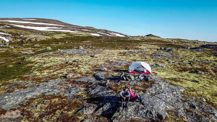 A couple sitting at the rock, enjoying the view on Eidfjord, Norway. They are camping in the wilderness. There is a tent behind them. Adventurous couple, living life to the fullest. Freedom and relax