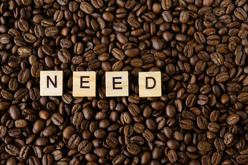 The word need is composed of individual letters on a background of roasted coffee beans. Top view, closeup