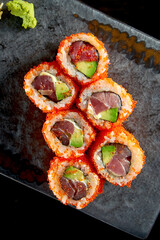 California sushi roll with tuna, avocado, cucumber and tobiko caviar served on a plate with wasabi and ginger. Isolation on a black background. Japanese food