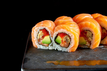 Appetizing red dragon sushi roll with salmon, eel, avocado and tobiko caviar, served on a ceramic plate with ginger and wasabi. Isolated on a black background. Japanese food