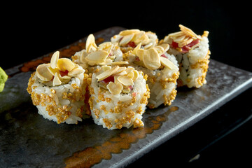 Delicious crispy sushi roll with tuna, peanuts, popcorn and cucumber, served on a ceramic plate with ginger and wasabi. Isolated on a black background. Japanese food