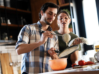 Husband and wife making pancakes at home. Young couple having fun in the kitchen..