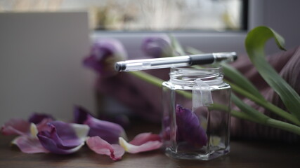 Słoik szklany przezroczysty z płatkami tulipanów fioletowymi na parapecie przy oknie w dzień 