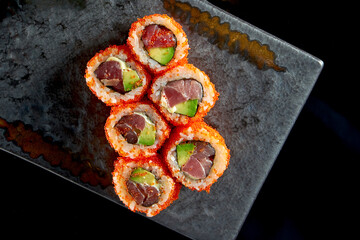 California sushi roll with tuna, avocado, cucumber and tobiko caviar served on a plate with wasabi and ginger. Isolation on a black background. Japanese food