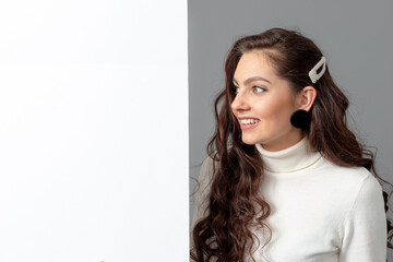 beautiful sensual woman with long curly hair shows a blank banner, isolated on gray, copy space
