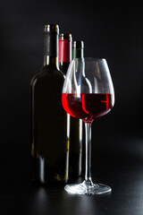 several different bottles of wine and a glass with red wine on a dark glossy background.