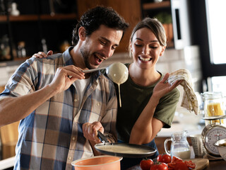 Husband and wife making pancakes at home. Young couple having fun in the kitchen..