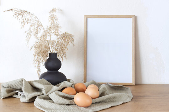 Spring, Easter still life. Empty picture frame mockups. Linen tablecloth, hen eggs. Reed grasses in a ceramic jug. Farmhouse, Scandinavian interior.