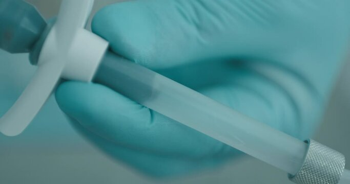 Close-up background a dentist hand in a blue disposable gloves that holding a elastomeric syringe while filling into it the impression paste.