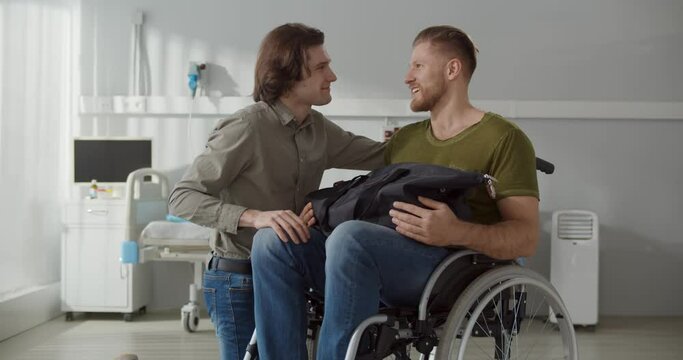 Young man taking boyfriend in wheelchair from hospital