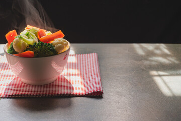Steam from hot-blanched vegetables in white blow on wood table by window in kitchen with morning sun light,Curry Blocks, Cauliflower and Carrots contain vitamins and fiber with good health benefits.