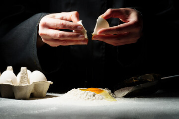 Dough preparation process on a dark . The woman breaks the egg and adds it to the flour.