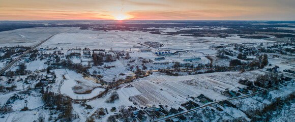 Panoramic view of red sunset in a winter evening over a village and field. Beautiful winter landscape from the air.