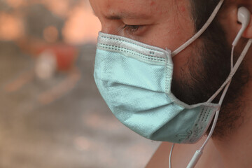 Close up of a man wearing headphones and a medical mask showing concept of daily life during the...