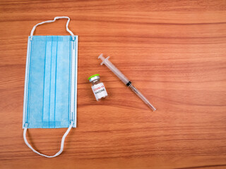 Top view of a vial covid-19 vaccine, syringe and facemask isolated on a wooden background. Covid-19 vaccination concept.