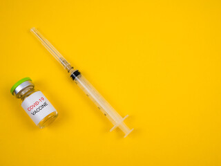 Top view of a vial covid-19 vaccine and syringe isolated on a yellow background. Covid-19 vaccination concept.