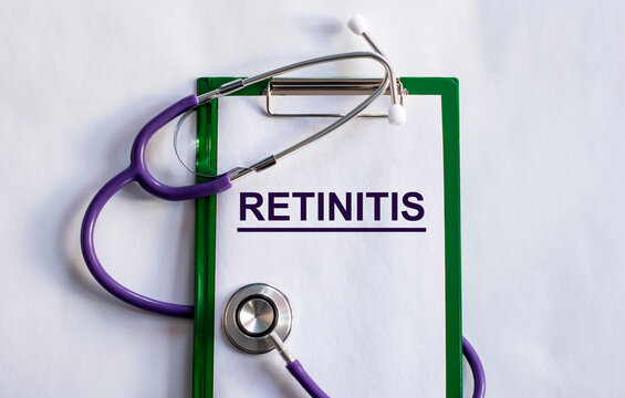 Notebook pade with word RETINITIS, on a table with a stethoscope.