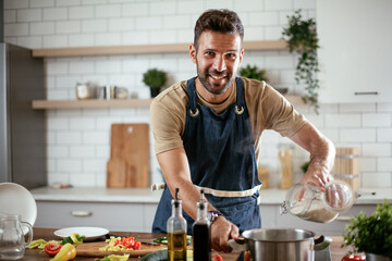 Happy smiling man preparing tasty meal. Young man cooking in the kitchen.