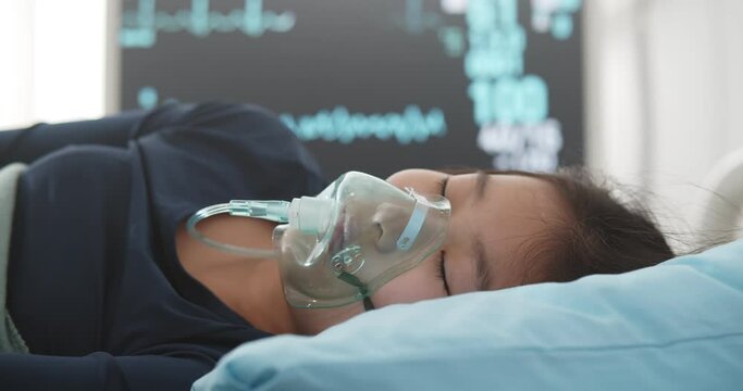 Asian girl suffering from pneumonia lying in hospital bed with oxygen mask