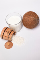 fresh coconut near wooden bowl with coconut flakes and glass of coco milk. isolated on white background. tropical nut