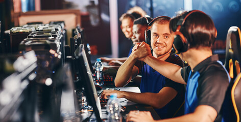 Professional cybersport team. Two happy male gamers shaking hands, celebrating success while...