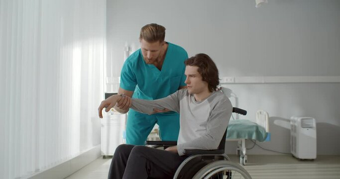 Nurse lifting arm of young paralyzed man sitting in wheelchair