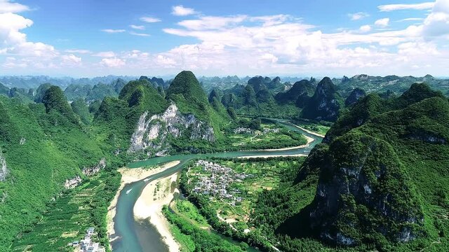 Bird's eye view of winding Li River, towns and peculiar karst landforms in Guilin, Guangxi under the blue sky and white clouds