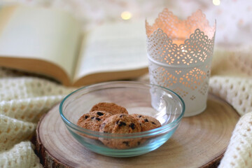 Bowl of chocolate chip cookies, lit candle and open book on a bed. Selective focus.