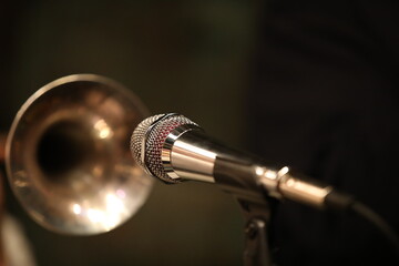 A shiny microphone in front of the blurry bell of a nightclub player's brass trumpet instrument.Art...