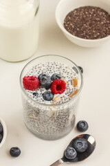 Chia seed pudding with blueberries, raspberries and pieces of mango, bowl of chia seeds and a bottle of milk on white background.  Quick and healthy meal concept. Stock photo, copy space