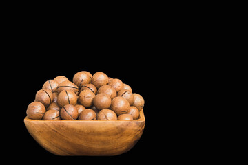 macadamia nuts in a wooden bowl close up on a black background