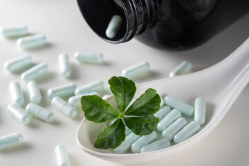 A spoon with a handful of capsules and a green leaf on white background. The concept of natural medicines.