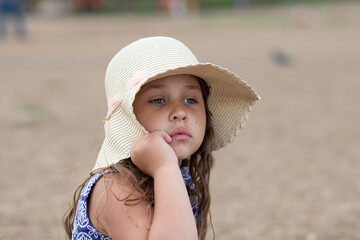 Little girl sitting and holding summer hat and beautiful dress on the beach