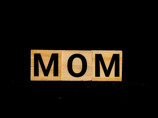 Wooden blocks alphabet "MOM" isolated with black background.