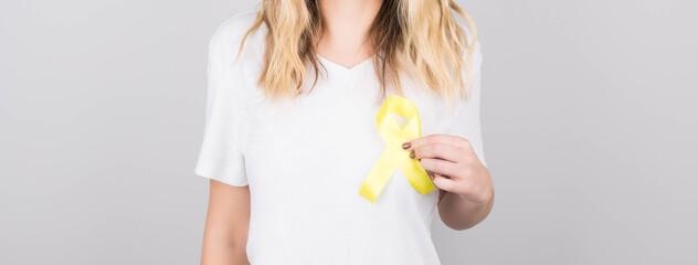 Young female in white t-shirt holding yellow ribbon awareness symbol for suicide, sarcoma bone cancer, bladder cancer, liver cancer and childhood cancer concept. Health care.