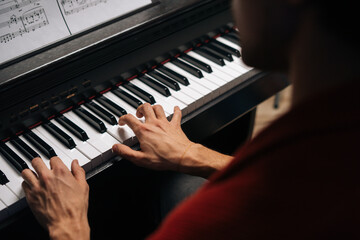 Top close-up view of hands of unrecognizable musician man playing on piano at home during lesson. Closeup back view of pianist male playing digital electronic synthesize. Concept of music education.