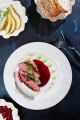 Duck breast with sweet pear on a white plate. Top view. Vertical photo. The concept of the restaurant menu. Blue background.