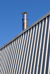 Close Up of Modern Industrial Building with Aluminium Cladding and Chimney against Blue Sky 