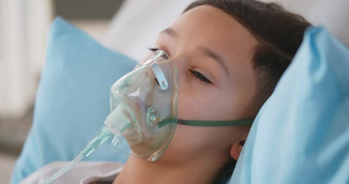 Sick african boy wearing oxygen mask lying in hospital bed