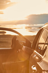 Fototapeta na wymiar Watching sunset. Close up of woman, female traveler pulling legs out of her car and enjoying amazing nature landscape in the evening