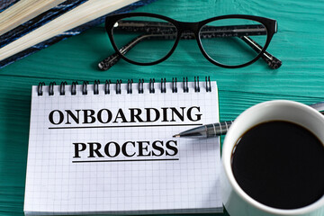 ONBOARDING PROCESS - words in a notepad on a wooden green background with a calculator, pen and glasses