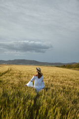 Fototapeta premium Feel it. Young woman in hat posing in a cultivated wheat field on a summer day