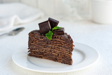 Piece of homemade chocolate crepes cake decorated with chocolate and mint on a white plate
