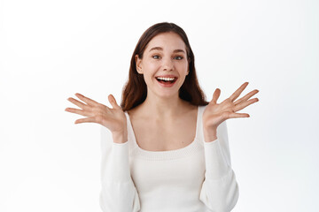 Lucky beautiful girl rejoicing from good news, laughing and smiling, raising hands up to celebrate joyful positive moment, hear good news, standing against white background