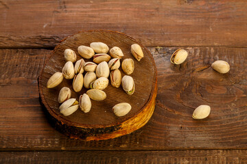 Pistachio nuts scattered on a round board on a wooden table.