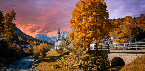 Fototapeta premium Scenic view on small parish church with mountains on background. Wonderful Evening scenery in Austrian Alps. Fantastic colorful Landscape with Mountains, picturesque sky and color trees during sunset.