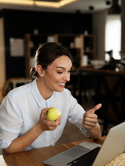 Happy woman using the laptop, having video call. Beautiful girl eating apple while talking with friends.