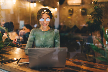 Fototapeta na wymiar Positive woman using laptop in cozy cafe